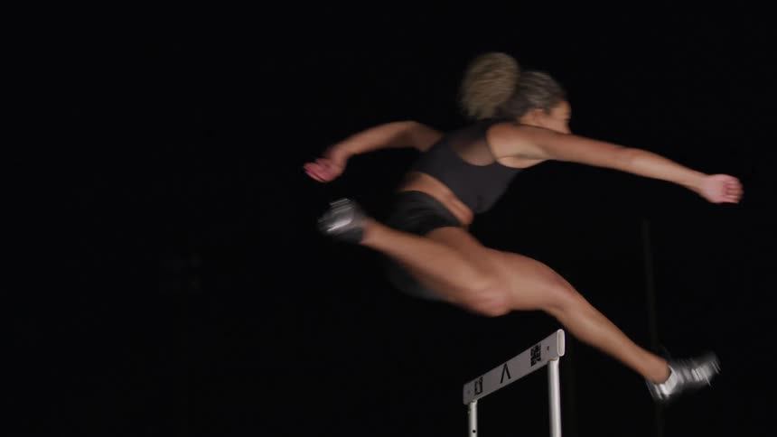 Female athlete jumps over a hurdle on the dark background