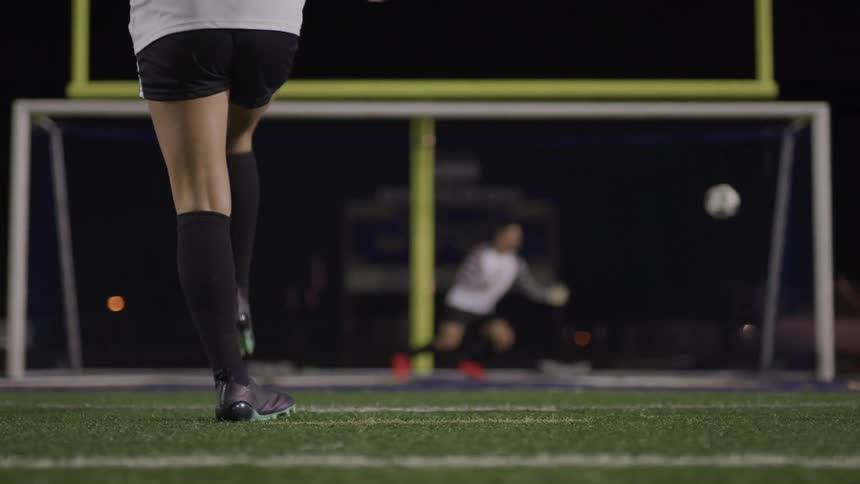 A soccer player kicks the ball into a net at night