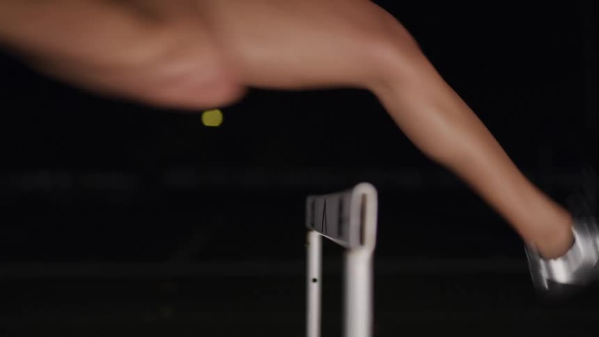 Female athlete jumps over a hurdle on the dark background