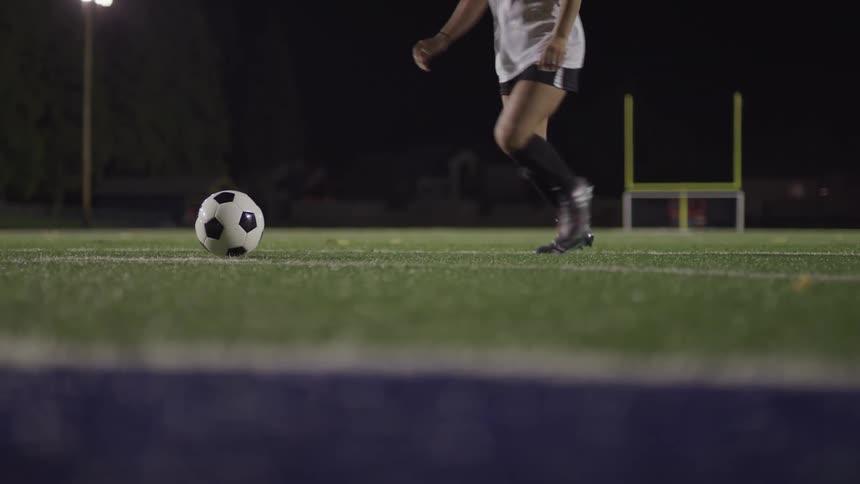 Female football player kicks a ball on the football field at night