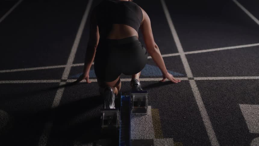Woman athlete waits for start of the long hurdle race in track and field stadium with an oval running track