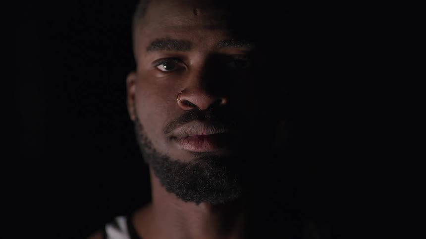 Black man looks at the camera on the dark background