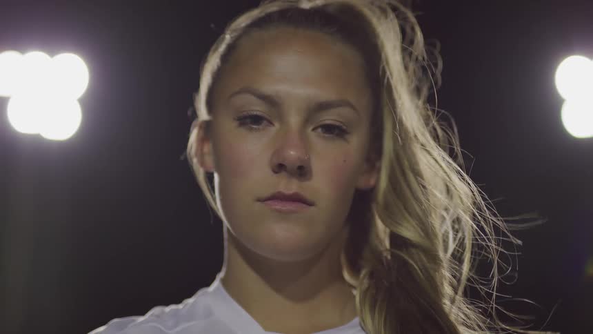 Blonde female footballer looks at the camera on the football field at night