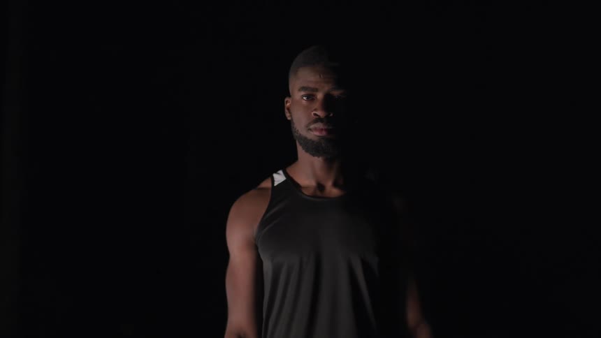 Black man wearing a fitness tank top in a dark room