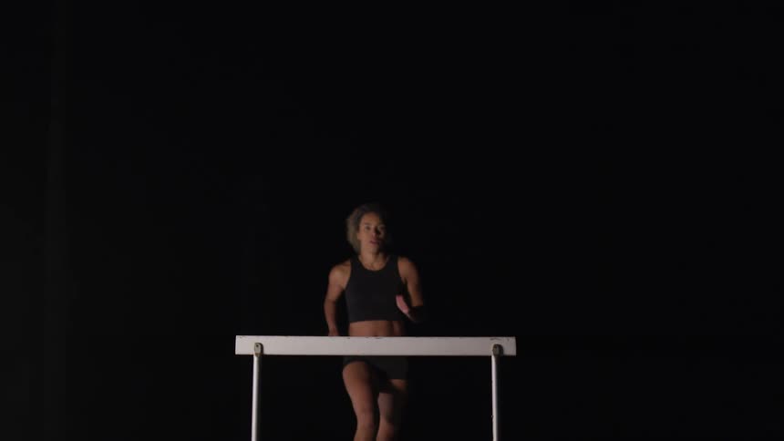 Close up of a female athlete jumping over a hurdle at night