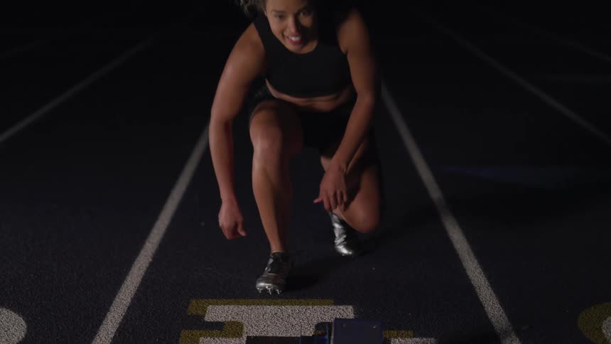 Woman athlete ties to shoe laces before running in a long hurdle race in track and field stadium with an oval running track