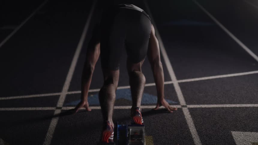 Runner takes off down dimly lit track from starting block