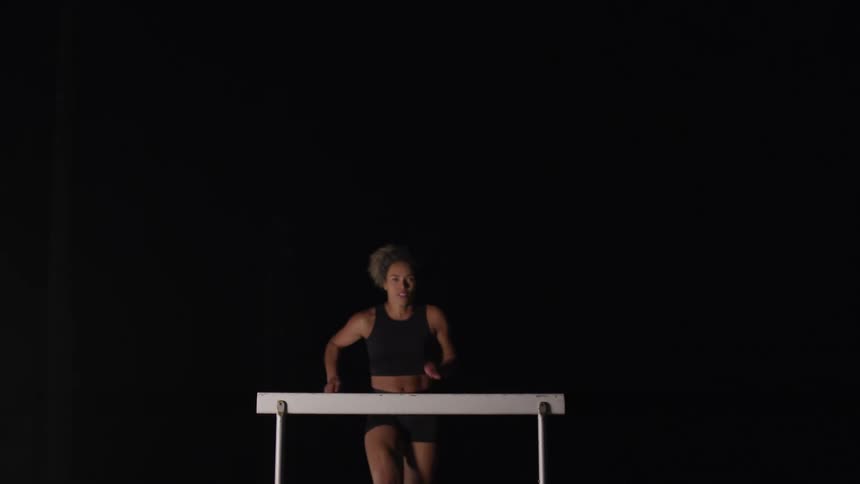 A woman runs and jumps over a hurdle