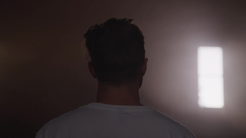 A man sits alone in a room and looks ahead