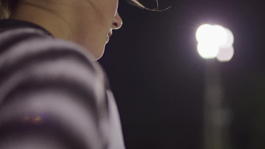 Female footballer stands and looks ahead on the football field at night