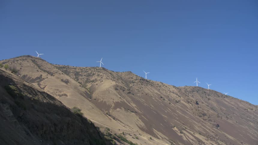 Wind turbines sit at the top of a tall dirt hill dotted with trees