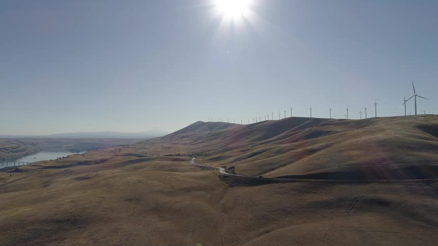 A truck travels on a road through dirt hills with still wind turbines along the ridge
