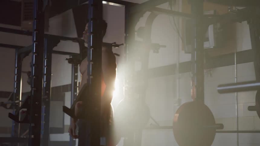 Shirtless sweaty man works out while the sun streams through window in the gym