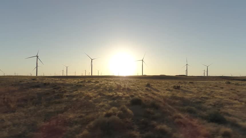 The sun is rising over windmills on a grassy plain