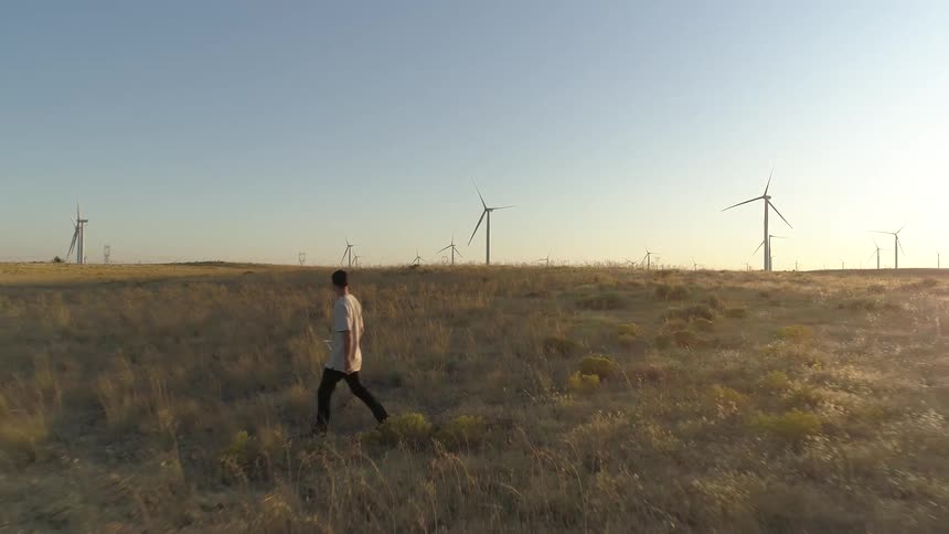 A man walks through a field filled with wind turbines that are not spinning