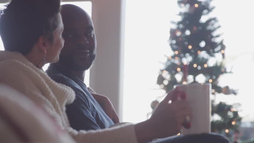 Couple sit together near christmas tree with coffee mug