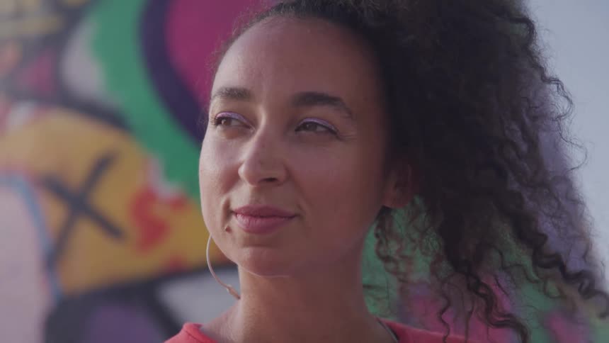 Latino woman listening to music on her earphone while sitting in front of a graffiti wall