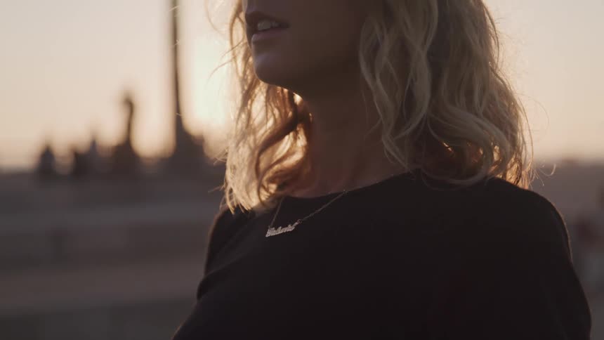 Blonde woman stands and looks around outdoors at sunset