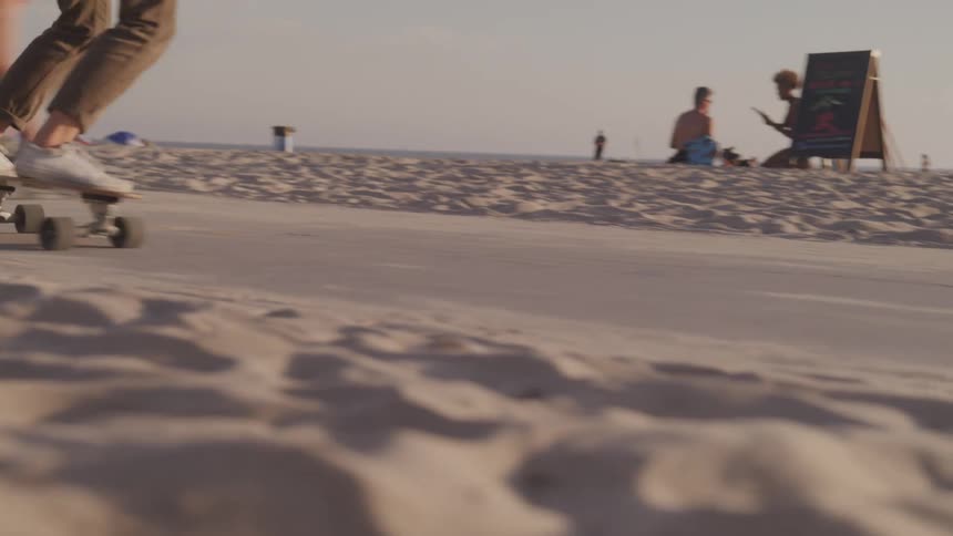A woman rides a skateboard on a beach sidewalk