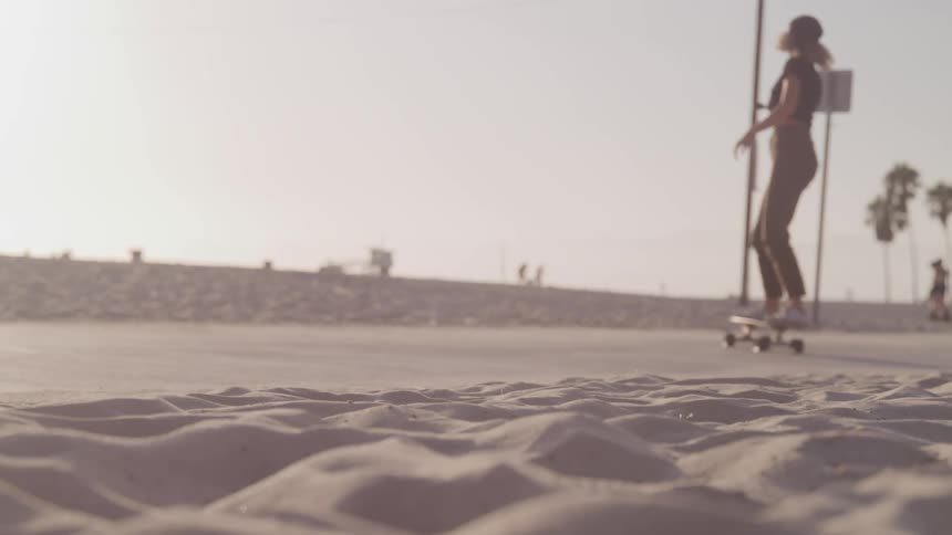 A teenager skateboards along the boardwalk while other people walk on the beach