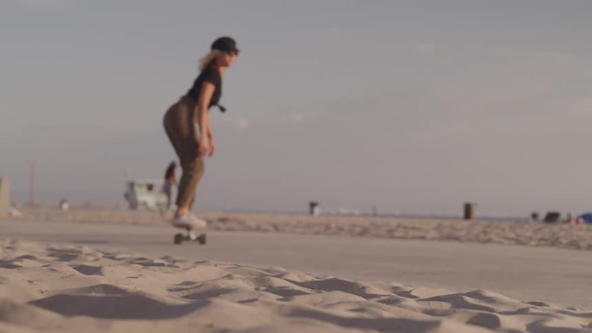 Woman rides on a skateboard as other women walk on the beach