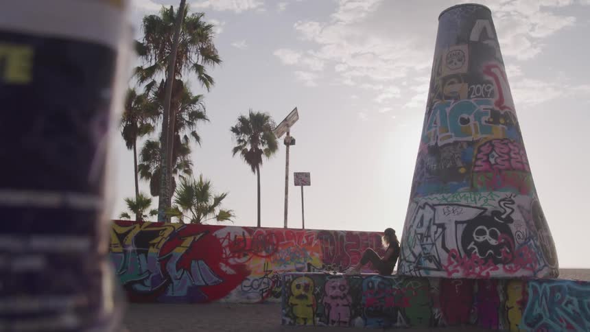 A woman leans up against a tower covered in graffiti