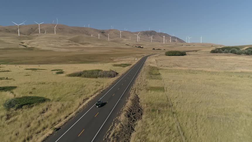 A car traveling down a desolate highway surrounded by hills and grass