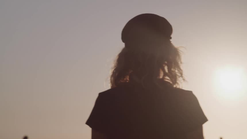 Woman wearing sunglasses and a black hat watches sunset