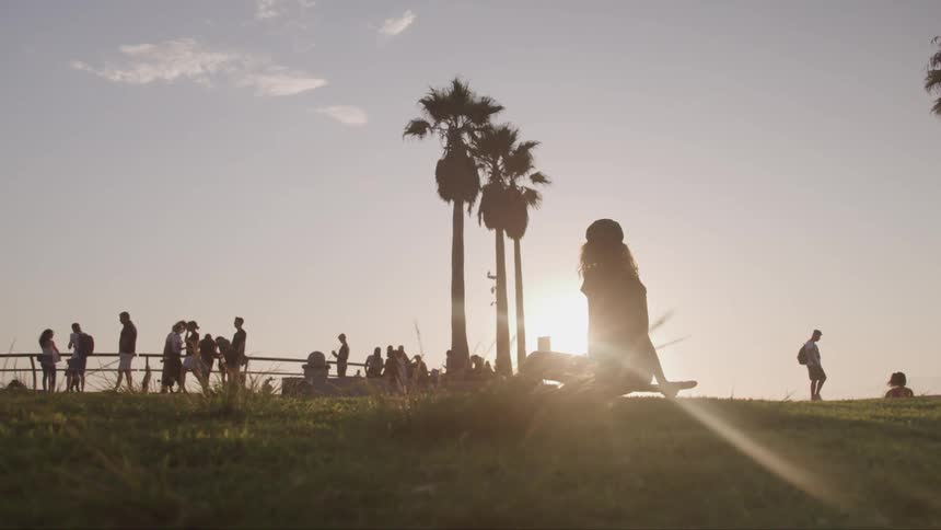 People walk and sit in a park at sunset