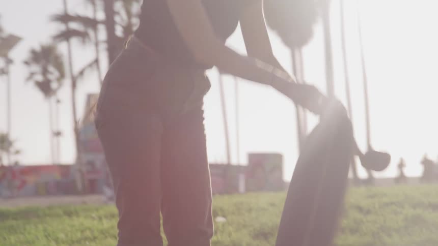 Woman sits to tie on shoes before getting up and skateboarding along sidewalk