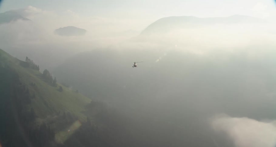 A helicopter is followed through the clouds over a grassy mountain range