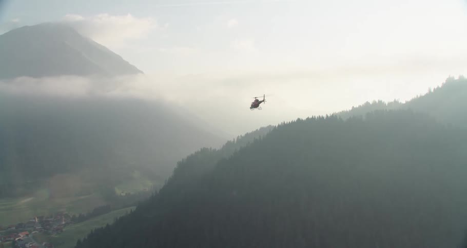 Helicopter flying close to mountains at cloud level near a small city