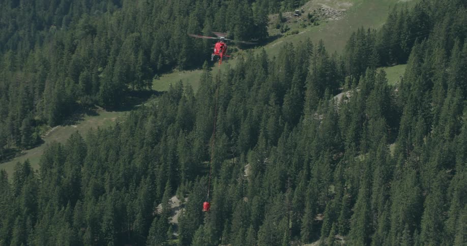Red helicopter flying over a forest carrying a red bucket