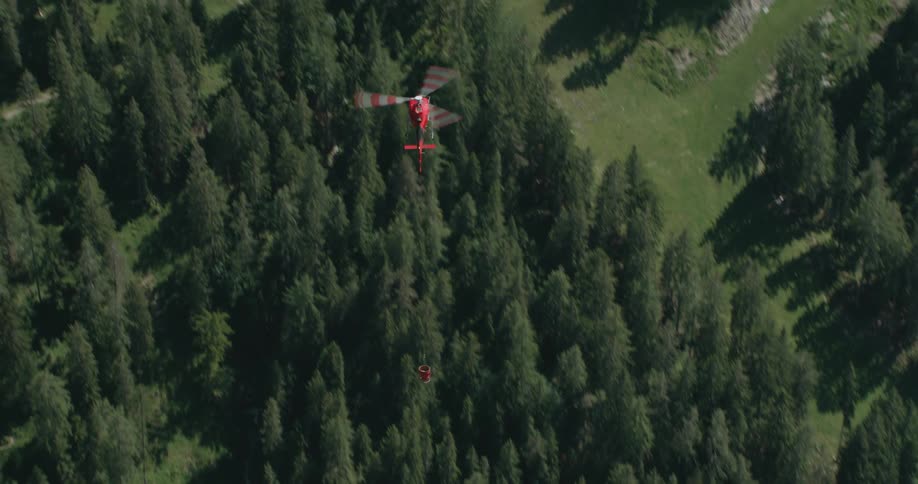 Red helicopter flying over the forest carrying a bucket