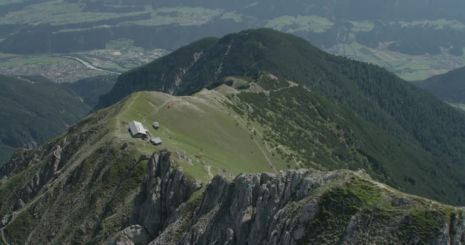 A vehicle travels a road toward a building on top of a large forest mountian