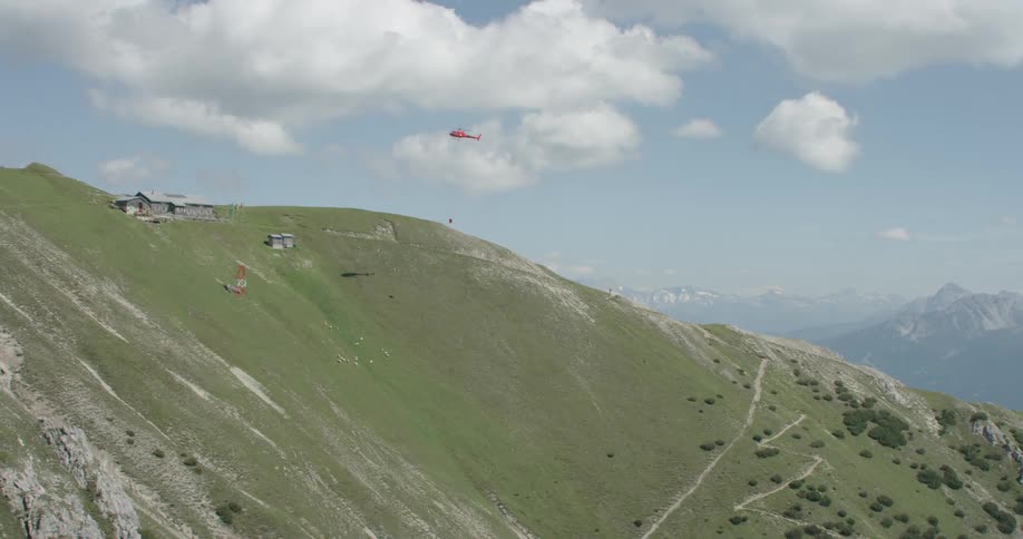 A helicopter flies towards a house with a basket lowered to the ground