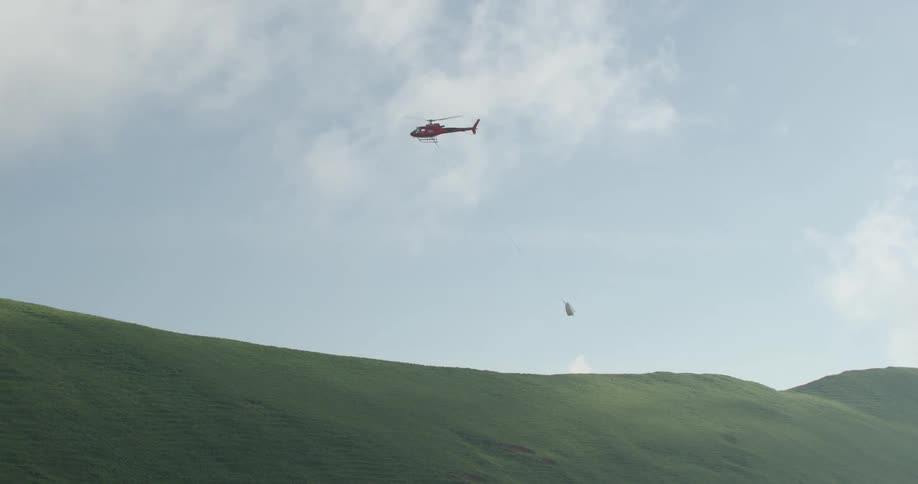 A helicopter carrying a water bucket flies over green hills
