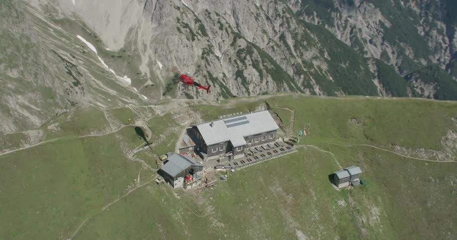 A helicopter hovers over a large building on top of a mountain