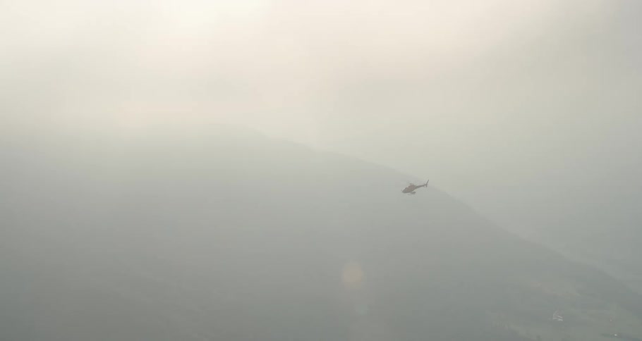 A helicopter flies through heavy clouds next to a barely visible mountain