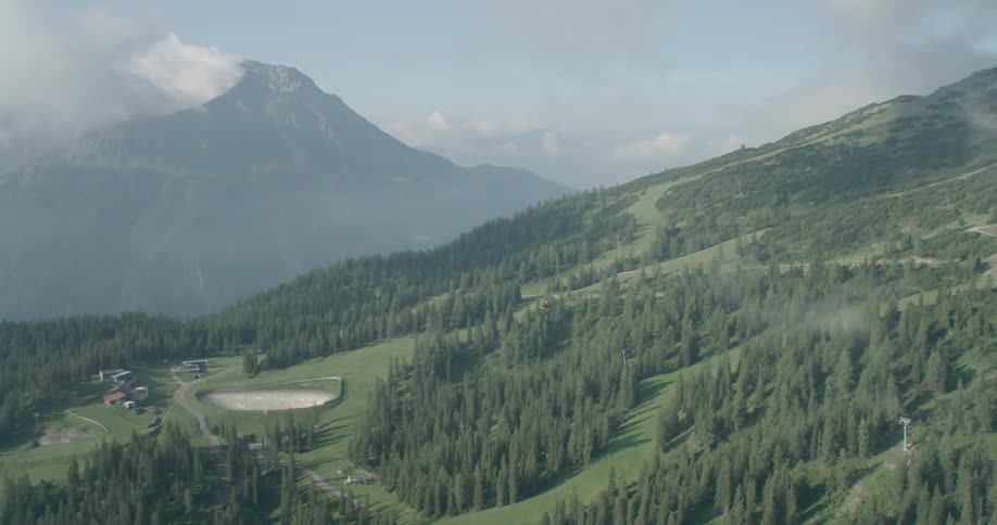 A forested mountain slope with a clearing containing a number of buildings