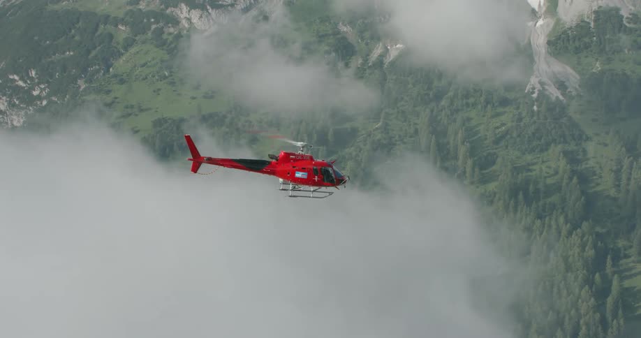 A rescue helicopter flies through the clouds over the mountain