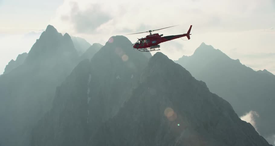 A red helicopter flying over a mountain ridge during the day