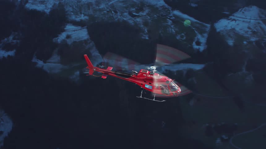 A red tirol helicopter flies over hilly and rocky terrain