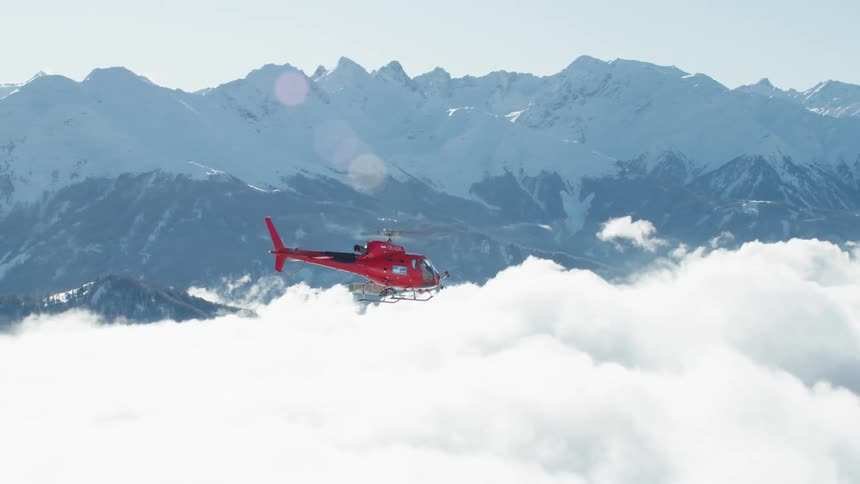 Red helicopter flying above the clouds close to mountains