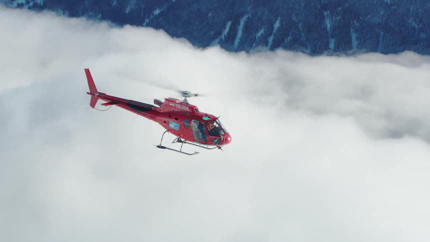 Search and rescue helicopter flies above the clouds and snow capped mountains
