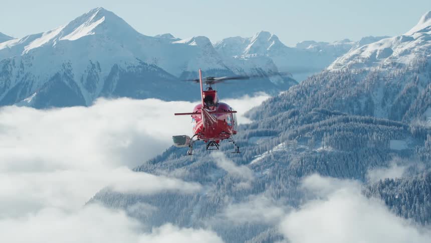 Red helicopter flying above the clouds close to the alps
