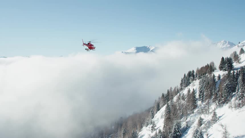 A helicopter flies over snow covered hills