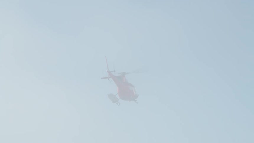 A helicopter flies over snowy hills