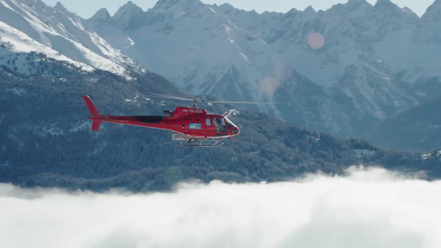 Red helicopter flying above clouds and close to the mountains