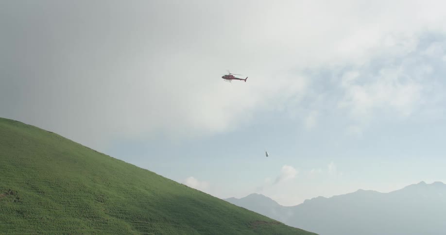 A helicopter flying in the sky toting a load with mountains in the background
